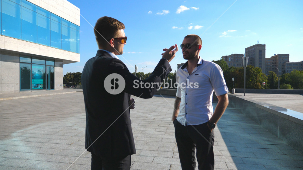 Two business men standing outdoor near office and talking. Businessmen meet and speaking outside in the city street with urban background. Communication of happy colleagues. Close up Dolly shot