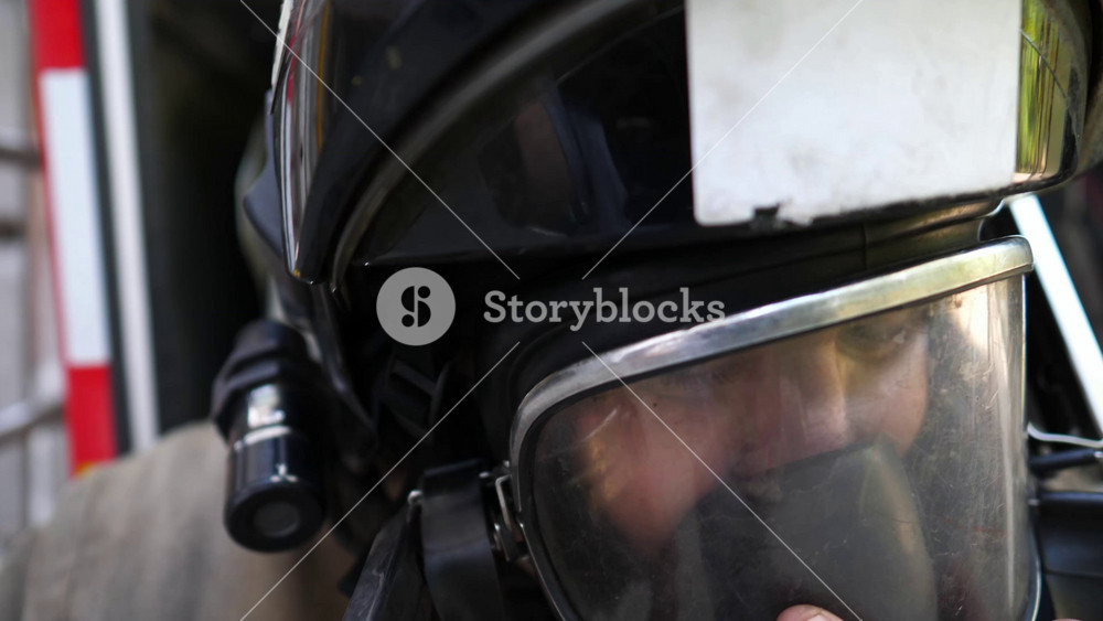 Professional firefighter putting oxygen mask against background of big truck. Young fireman in full equipment near fire engine ready to work. Concept of saving lives and heroic profession. Slow motion