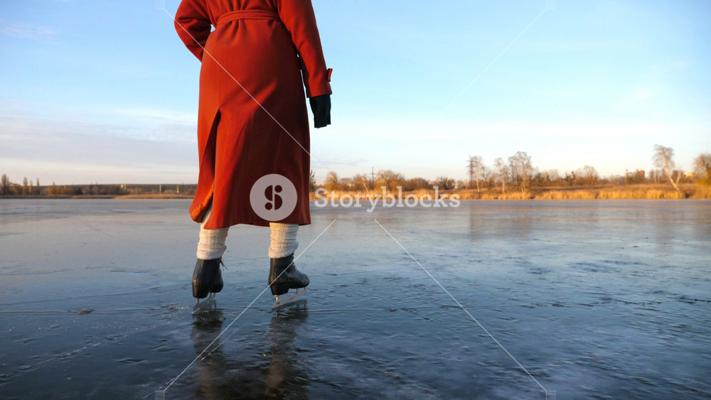 Woman in coat and figure skates sliding on ice on frosty winter day. Girl skating on frozen river or lake. Lady enjoying sport and improves skills in cold weather. Active leisure at wintertime. Slowmo.