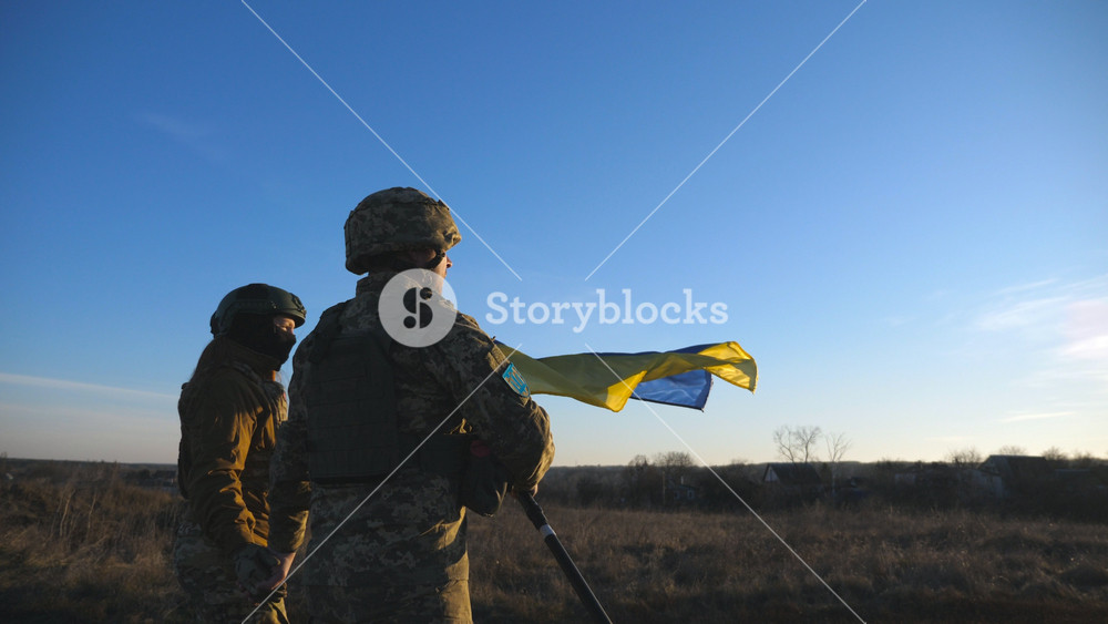 Ukrainian army soldiers stands outdoor at sunset time and waves flag of Ukraine. People in military uniform lifted up flag against blue sky. Victory at war. Resistance to russian invasion. Slow motion.