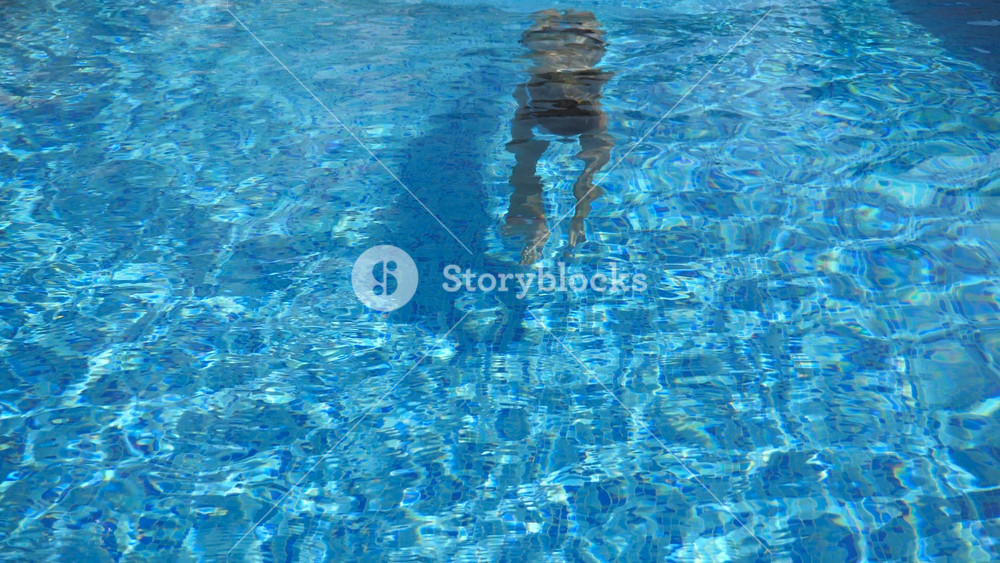 Woman swim under the water and emerges on the surface. Young beautiful girl swimming in pool. Summer vacation or holiday concept. Slow motion