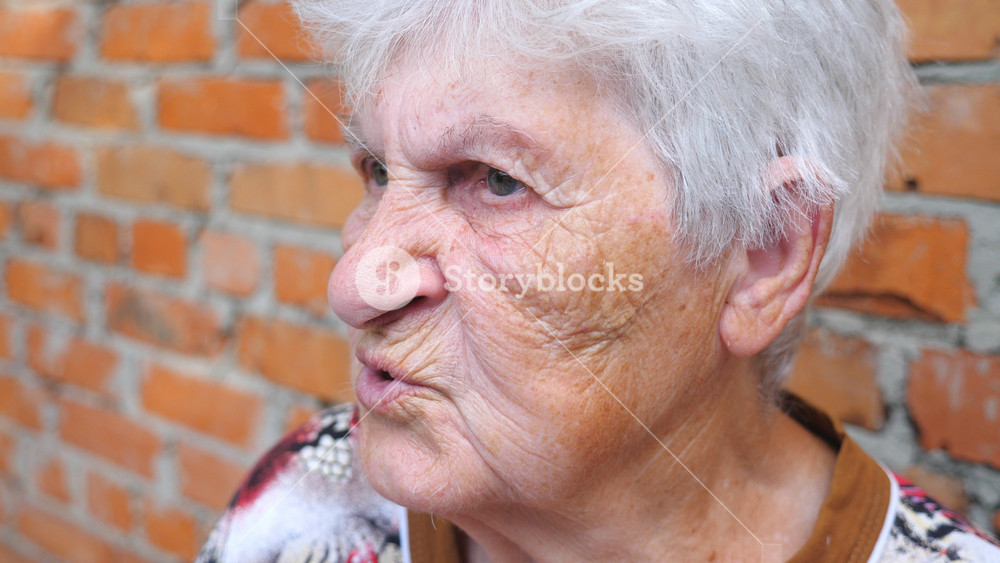 Grandmother sitting outdoor and talking with somebody. Portrait of elderly woman with serious facial expression telling story. Grandma communicating with someone. Slow motion Close up