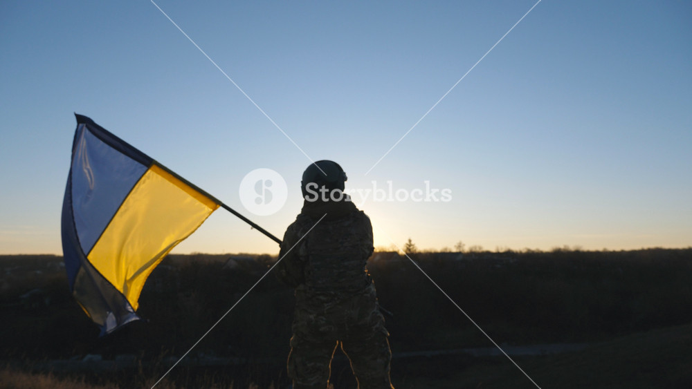 Female ukrainian army soldier lifting national banner in hill. Young woman in military uniform waving flag of Ukraine against background of sunset. Victory at war. Resistance to russian invasion.