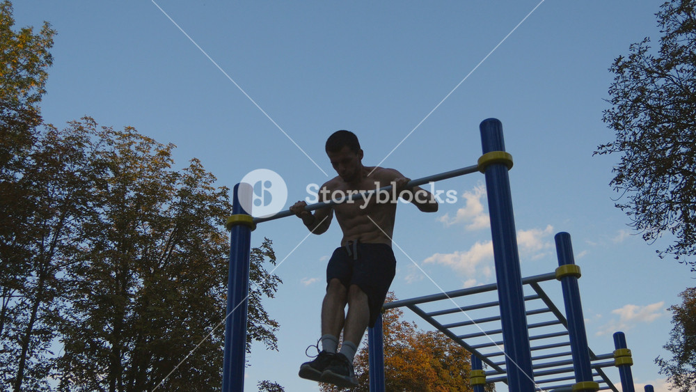 Strong muscular man doing muscle ups in a park. Young athlete doing chin-ups on horizontal bars outdoor. Fitness muscular man training outside in summer. Sportsman pulling up. Workout sport lifestyle.