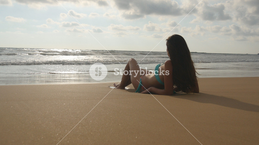 Beautiful young woman in bikini lying on golden sand on sea beach and relaxing during summer vacation travel. Tanned girl sunbathing on