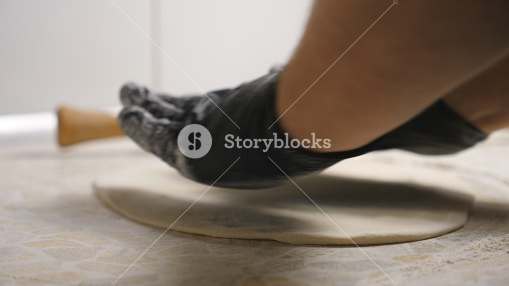 Male arms of cook in gloves forming pastry on a wooden surface at cuisine. Hands of chef shaping floured dough for pizza on a kitchen table at restaurant. Concept of preparing food. Close up Slow mo