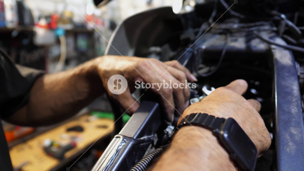 Male hands of repairer fixing moto engine at workshop. Arms of professional mechanic repairing detail of motorcycle at workplace. Adult repairman mending vehicle motor at garage. Maintenance service.