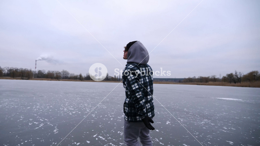 Guy skating on frozen river at cloudy day. Young man shod in figure skates sliding on ice surface outdoor. Sportsman training at lake in winter cold weather. Active leisure at wintertime. Slow motion.