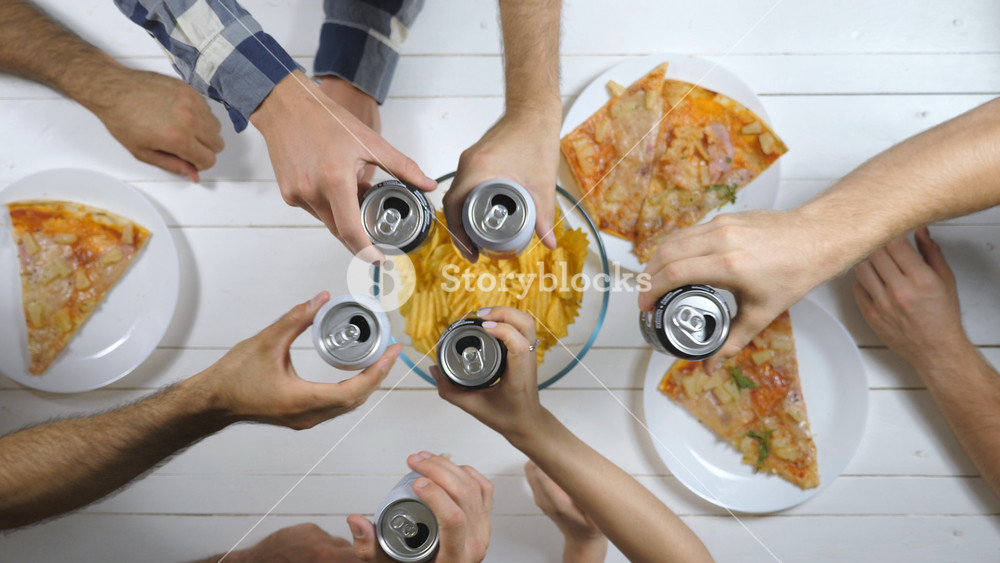 Male and female hands clicking aluminum cans with soda on wooden table background. Group of best friends sitting at the desk and toasting