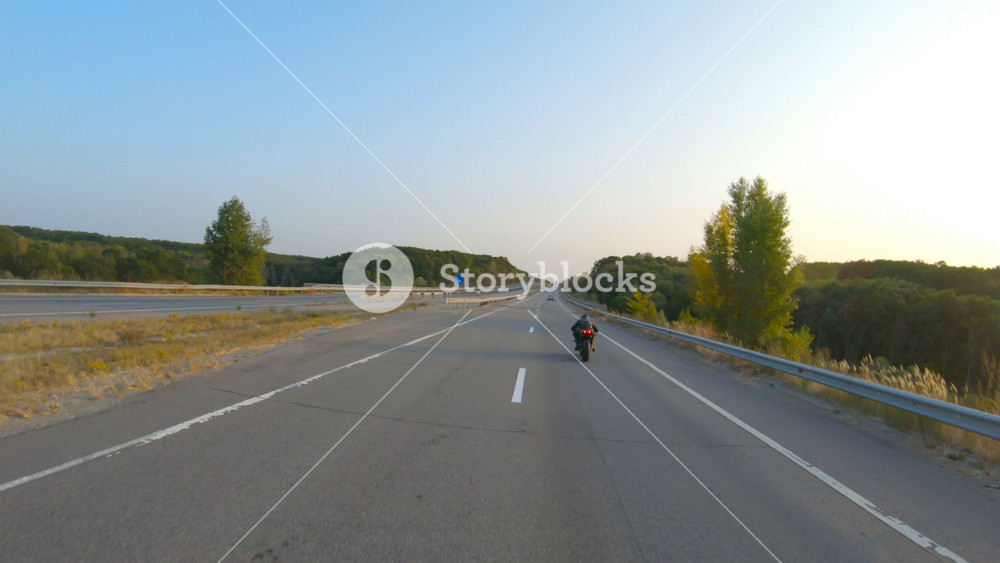 Biker is driving motorbike during road trip at autumn sunset time. Man ride fast on modern sport motorcycle at highway. Motorcyclist racing his bike on country road. Concept of adventure. Aerial shot.