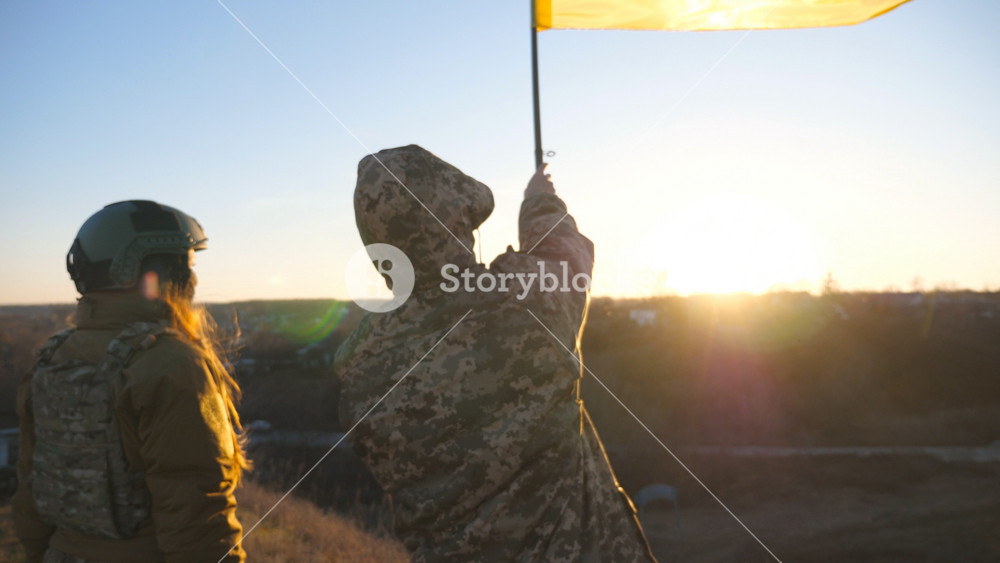 Soldiers of ukrainian army holding waving flag of Ukraine. Military people lifted up flag at the hill as victory against Russian aggression. Concept of invasion resistance and end of war. Slow motion.