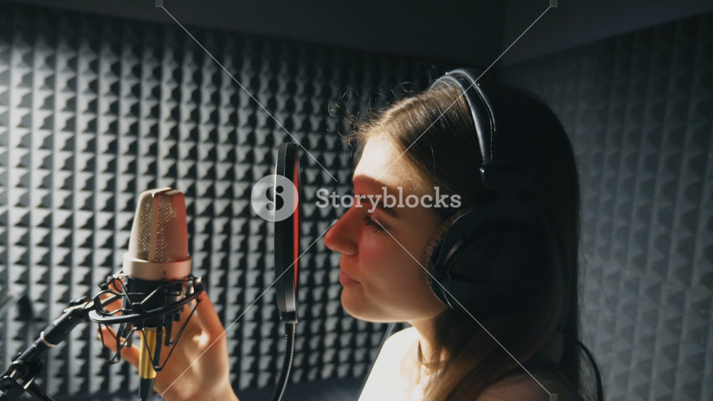 Profile of beautiful girl singing in sound studio. Young female singer emotionally recording new song. Woman sings to microphone. Working of creative musician. Show business concept. Slow motion