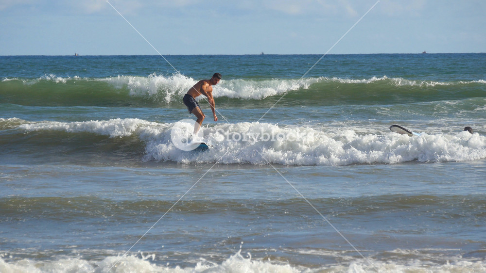 Close up of young athletic guy paddling out at blue ocean wave and learning to surfing on sunny day. Sporty man riding on surfboard at sea. Beautiful seascape at background. Vacation concept.