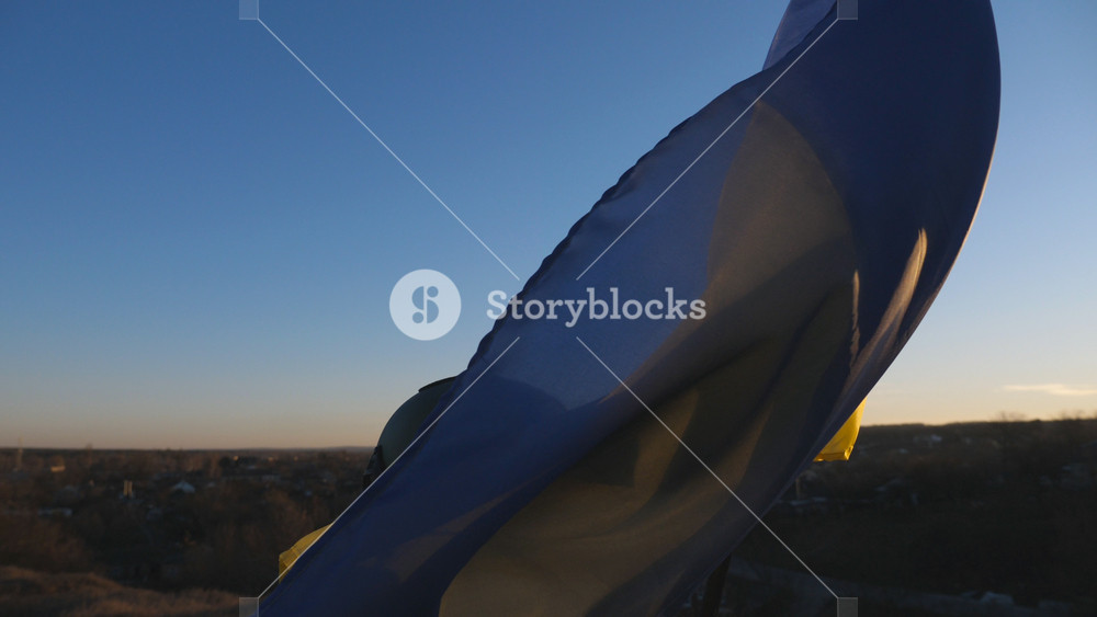 Female ukrainian army soldier lifting national banner at hill. Woman in military uniform waving blue-yellow flag against background of sunset. Victory of war. Invasion of territory Ukraine. Dolly shot.
