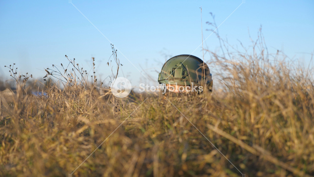 Military soldier in outfit and helmet hiding in a trench during shelling and watching the enemy army. Ukrainian soldier looking from the shelter hides behind a hill from attack. War in Ukraine