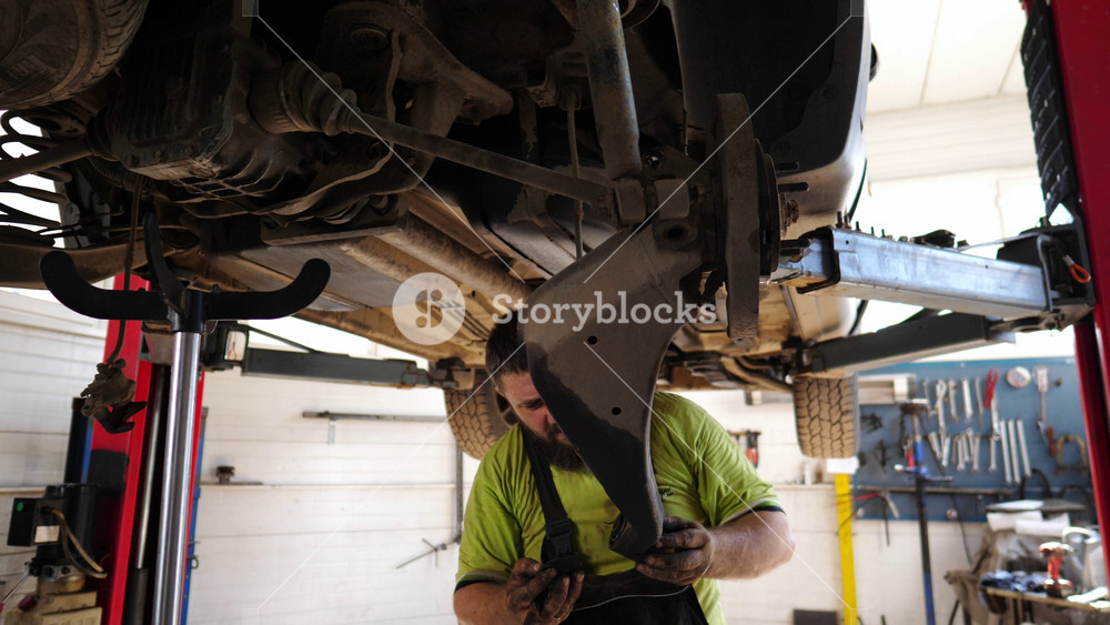Auto mechanic removing part of vehicle at workshop. Professional repairman working underneath a lifting car at garage. Male repairer fixing automobile at workplace. Concept of regular maintenance.