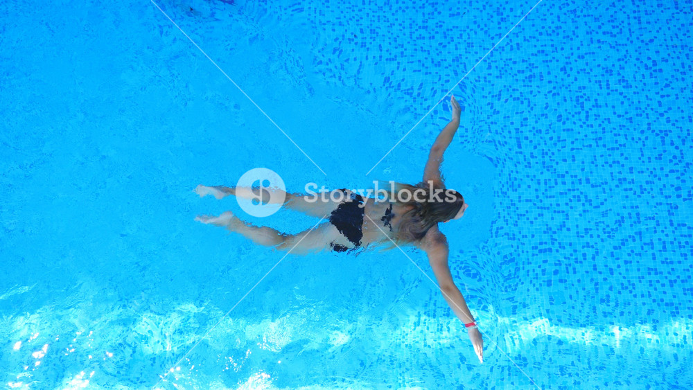 girl in black swimsuit swimming across pool of luxury hotel. Young woman relaxing in warm water of basin and enjoying summer vacation. Lady