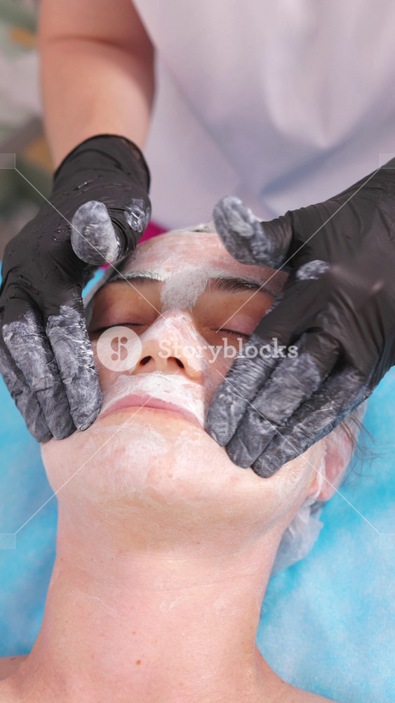 Middle aged female receiving facial massage in beauty salon. Anti aged massage and skincare concept. Hands of cosmetology specialist making facial lifting massage in SPA Salon.