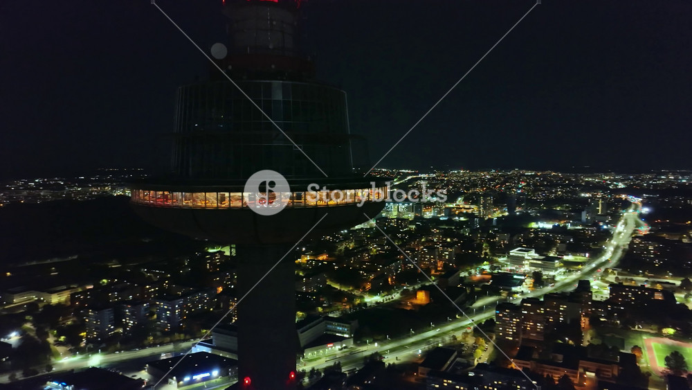 The Vilnius TV Tower glows with red lights at night, standing tall against a dark sky. The camera pans, revealing the lit cityscape of Vilnius, Lithuania.