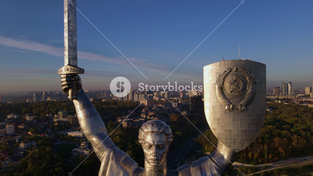 Aerial view of the Mother Ukraine monument in Kyiv, Ukraine, with smooth motion around its sword and shield, cityscape, and Dnipro River in the background.