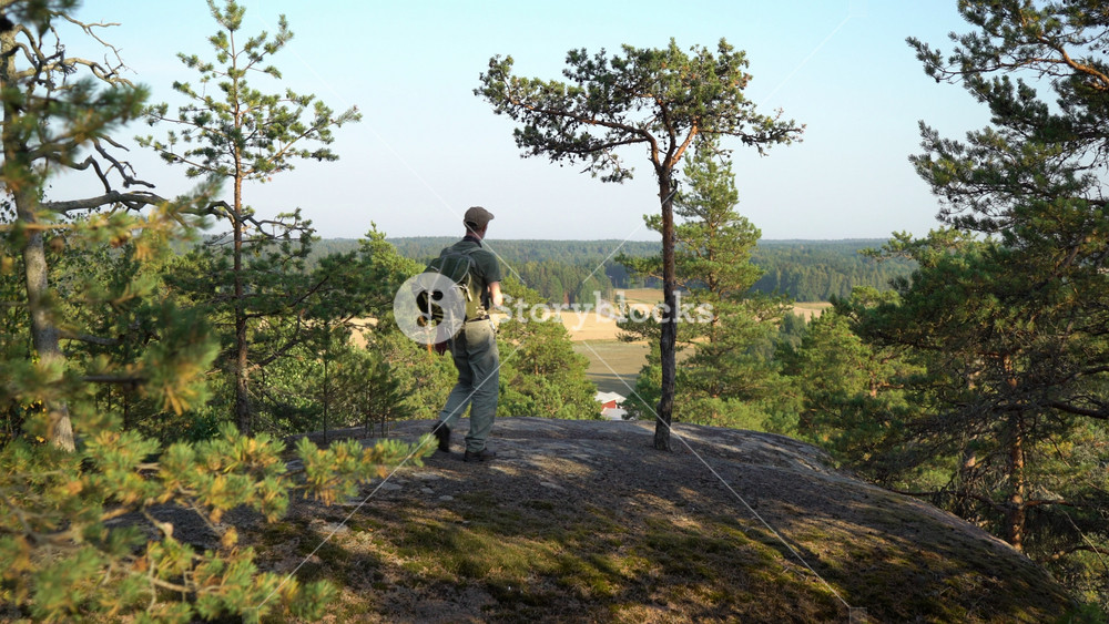 Mature man with hiking equipment walking in mountain forest in Finland and photographing breathtaking northern landscapes with an old