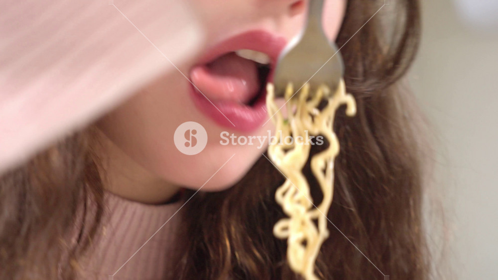 A teenage girl with long brown hair is eating instant ramen noodles. Unhealthy fast food choices, artificial additives, and the importance