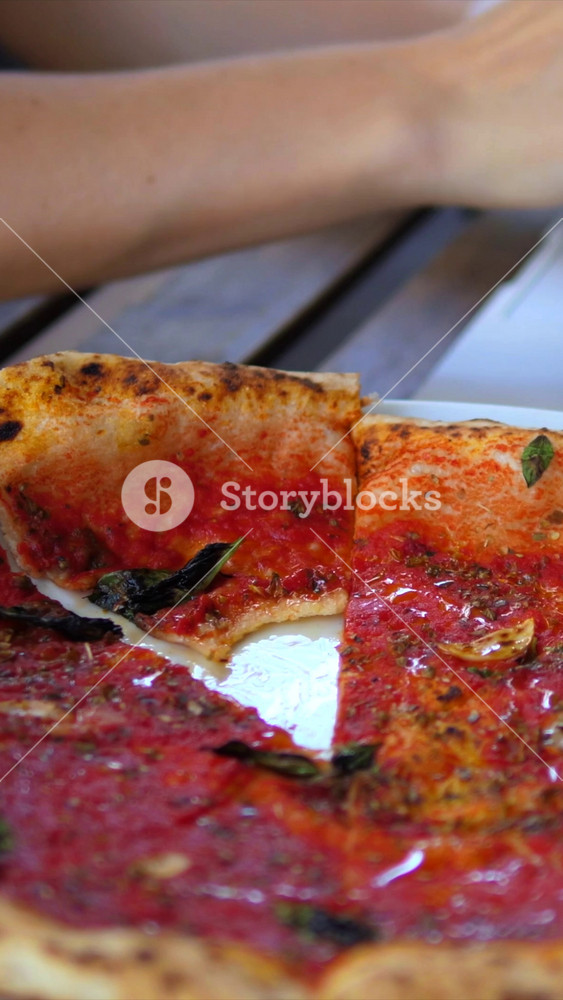Close up view of a person taking a slice of delicious marinara pizza from a plate on a wooden table, enjoying an italian meal at a